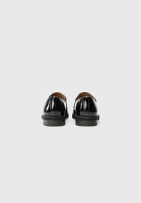 Black patent leather shoes with a smooth finish, rounded shape, low heel, and subtle stitching details along the back.