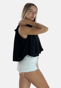 Top corto nero senza maniche con un design fluido e dettagli arricciati sulle spalle, abbinato a pantaloni corti in denim bianco sfilacciati. Texture liscia.