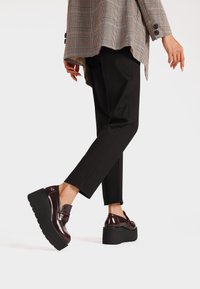 Scarpe in pelle lucida bordeaux con una spessa suola nera a piattaforma. Caratterizzate da una finitura liscia e un dettaglio con fibbia sicura. Indossate con pantaloni neri.