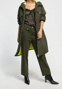 Parka acolchada en verde oliva con forro amarillo neón, combinada con una camiseta de leopardo y pantalones de corte recto en verde oliva. Botines negros de tacón puntiagudo.