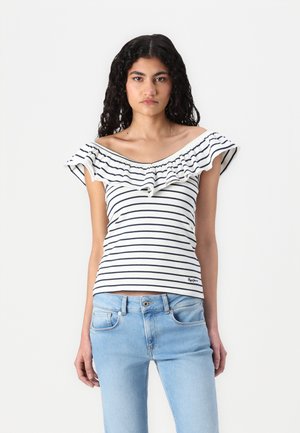 Top a spalla scoperta con righe, dotato di scollatura a volant, caratterizzato da righe blu navy su sfondo bianco. Indossato con jeans in denim blu chiaro.
