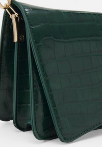 Grön fejk-krokodilhandväska med guldfärgade detaljer, som har en strukturerad design och vackert sydda kanter.