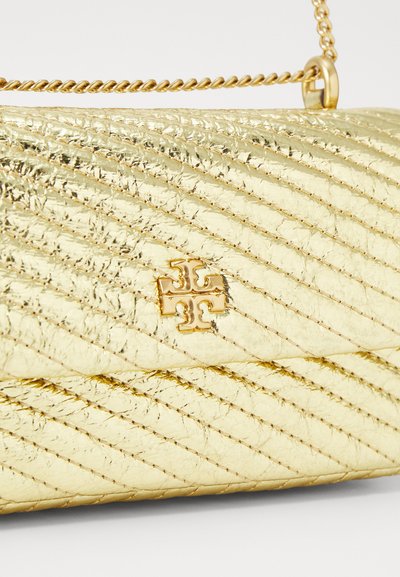 Bolso acolchado dorado con costura diagonal y un logo. Presenta una correa de cadena y una superficie texturizada y brillante.