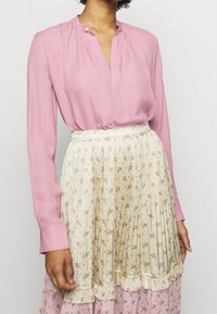 Rosa långärmad blus med en krage med knäppning, i kombination med en plisserad krämfärgad kjol med små blommönster och volangkant.