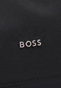 Tissu noir texturé avec un logo « BOSS » en argent métallique. Le design est élégant avec peu de détails de couture.