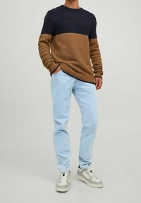 Suéter de punto con parte superior texturizada en color marino y sección inferior marrón, combinado con jeans de color azul claro y zapatillas grises.