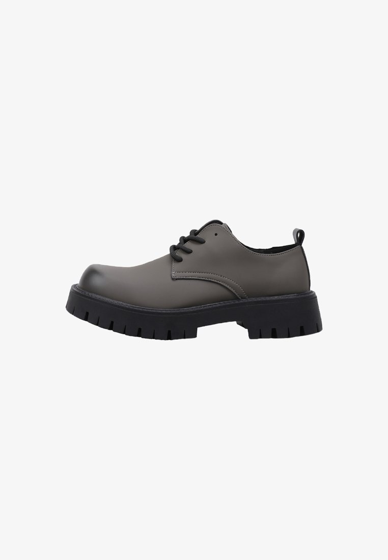 Zapato de cuero gris oscuro con cordones, suela gruesa negra y tirador en el talón, vista lateral sobre fondo blanco.