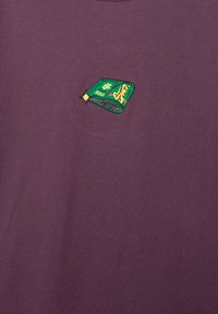 Kortærmet, lilla bomulds t-shirt med et grønt broderet design af en bunke penge med en "$200" etiket og stjerne accenter.