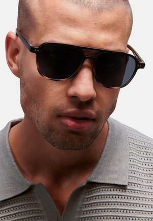Gafas de sol negras con lentes oscuros y forma rectangular. Montura de plástico de color marrón y negro con un diseño patterned, que presenta pequeños acentos metálicos.