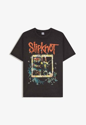 Schwarzes Slipknot-Band-T-Shirt mit verwaschenem orangefarbenem Logo über einer Grafik eines Ziegenkopfs und abstrakten Formen, umgeben von kleinen weißen Fliegen.