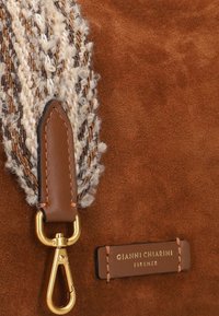 Borsa in suede marrone con una tracolla intrecciata testurizzata in fili crema e marrone, accessori in oro e un'etichetta in pelle con logo.