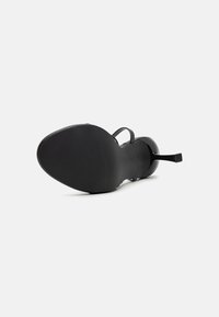 Mustmustel oleva must sandaal ilma kandega ja siledat pinda. Omab õhukesi rihmasid ja tekstureeritud kummist tallat, mis tagavad haakumise. Minimalistlik disain.