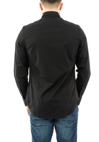 Camisa negra de manga larga con una textura suave, que presenta un collar estándar y puños abotonados, combinada con jeans de mezclilla azul.