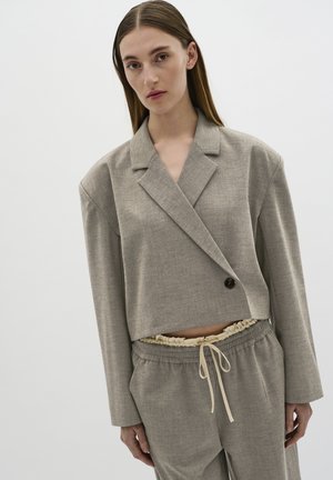Hellgrauer, taillierter Blazer mit einem Knopf, der aus einem strukturierten Stoff besteht und über kunstvolle Revers verfügt, kombiniert mit passenden grauen Jogginghosen mit Kordelzug.