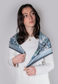 Silk scarf med blomstermønster i blå og grønne nuancer med stribede kanter. Båret draperet over en hvid sweater, hvor teksturen fremhæves.