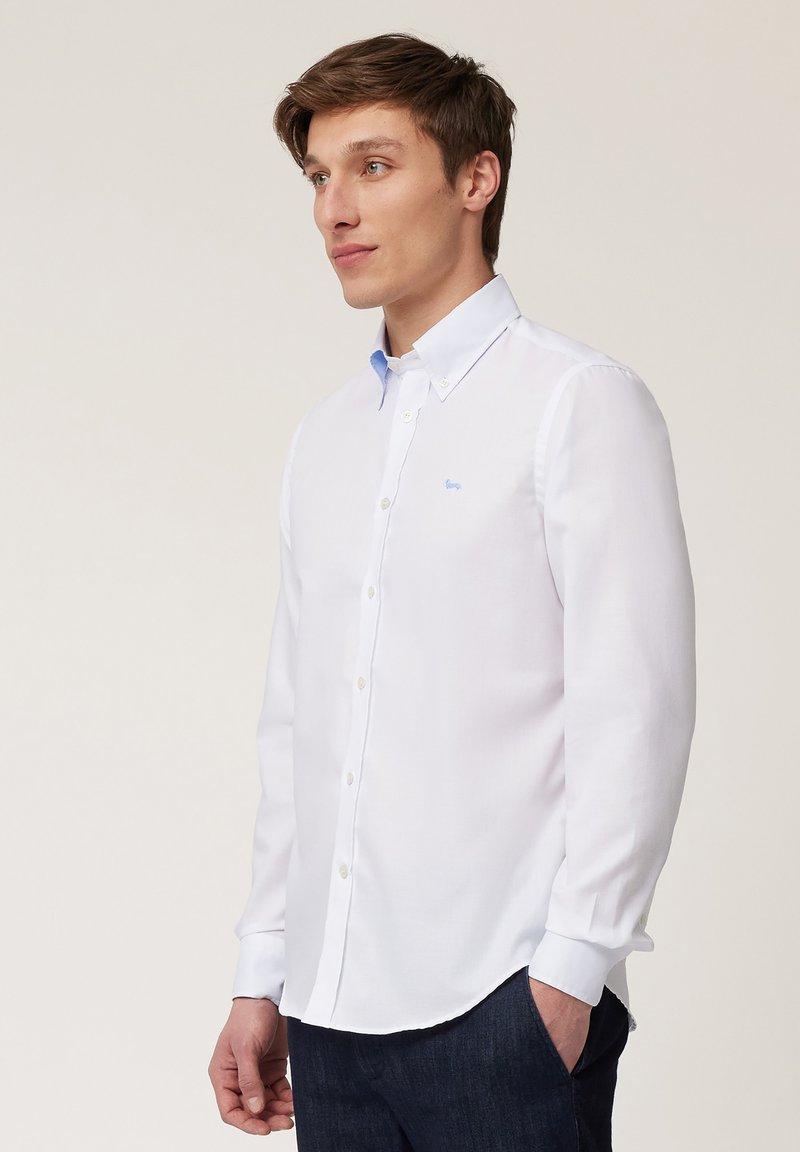 Chemise blanche à boutons avec un col bleu clair. Présente un petit logo bleu sur la poitrine. Manches longues et design à ourlet courbé.