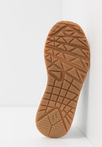 Schoenenzool met een getextureerd oppervlak van gomrubber en driehoekige loopprofielen, ontworpen voor grip. Witte zijkant met minimale details.