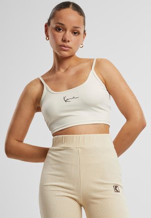 Haut court crème à fines bretelles, orné d'un logo noir emblématique. Associé à un pantalon côtelé beige taille haute.