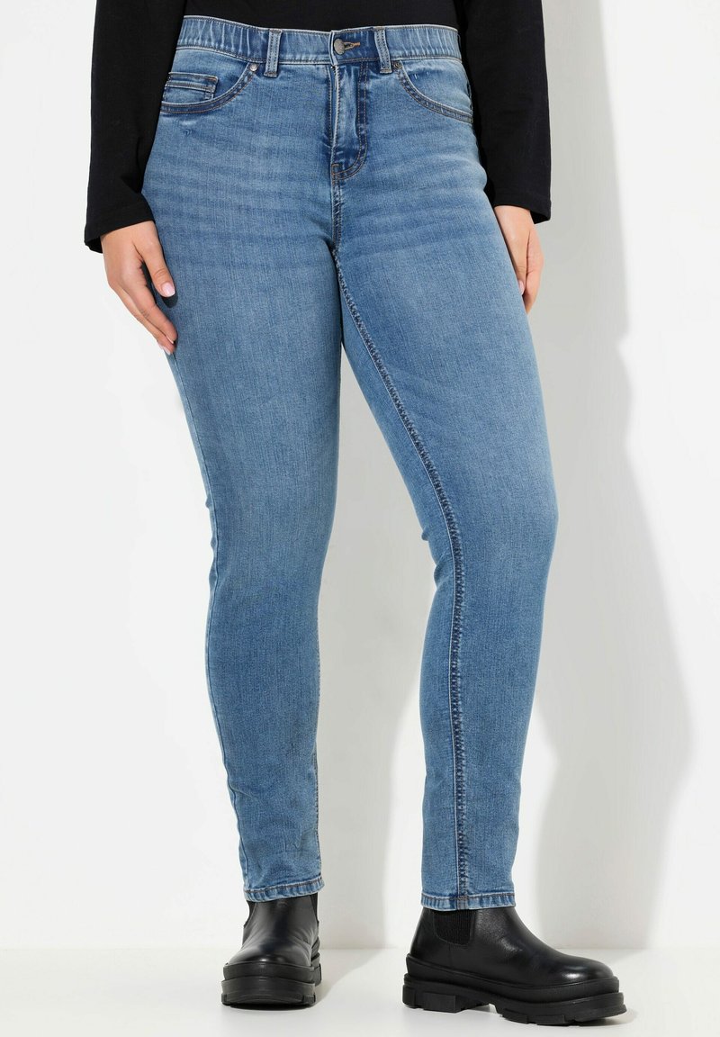 Jeans de mezclilla azul ajustados con una cintura de altura media, diseño clásico de cinco bolsillos y dobladillo doblado, combinados con botas negras hasta el tobillo.