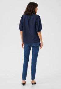 Blusa a rayas azul marino con mangas abullonadas, combinada con jeans azules ajustados y sandalias de tacón negro. La textura es suave, con un diseño estructurado.