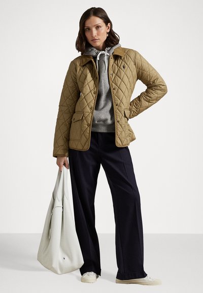 Beige gewatteerde jas met contrasterende tan kleur kraag, knoopsluitingen en twee voorkeuren; gecombineerd met een grijze hoodie, marineblauwe broek en een witte tas.
