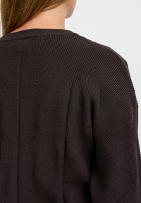 Mörkbrun stickad tröja med strukturerade mönster, ribbade detaljer och en avslappnad passform med vid halsringning och sänkta axlar.