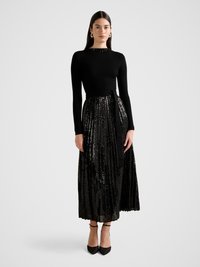 Black ribbed long-sleeve top paired with a pleated midi skirt covered in sequins. The silhouette is cinched at the waist with a black sash.