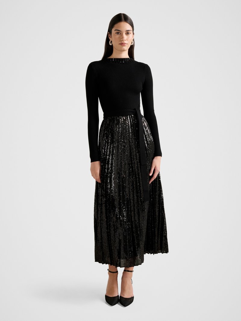 Black ribbed long-sleeve top paired with a pleated midi skirt covered in sequins. The silhouette is cinched at the waist with a black sash.
