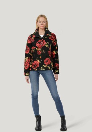Schwarze Fleecejacke mit leuchtendem roten und grünen Rosenmuster, ausgestattet mit einem hohen Kragen und einem Reißverschluss, kombiniert mit blauen Skinny Jeans.