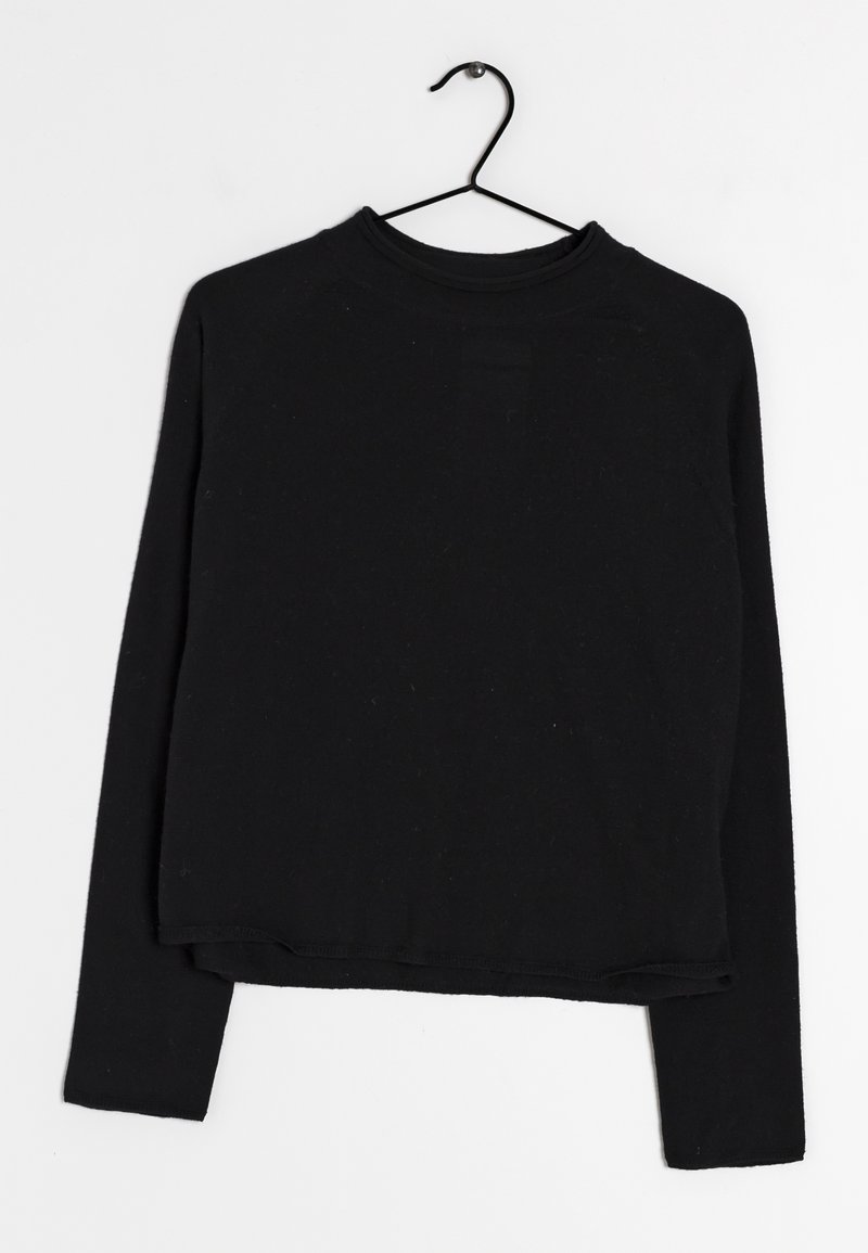 Haut noir à manches longues et coupe courte avec encolure ronde suspendu à un cintre en fil de fer noir sur un fond blanc.