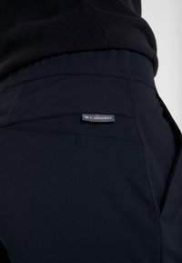 Black fabric pants with a smooth texture, featuring a Columbia label on the back pocket and a sleek design.