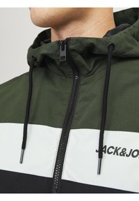 Giacca con cappuccio verde scuro, caratterizzata da strisce orizzontali bianche e nere. Dotata di cerniera, coulisse e logo stampato del marchio.