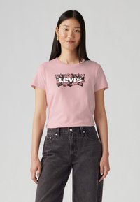 T-shirt en coton rose avec un design de logo floral noir de Levi's. Associé à un jean en denim noir taille haute, créant un look décontracté.
