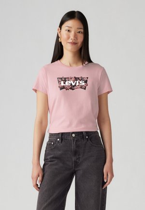 T-shirt en coton rose avec un design de logo floral noir de Levi's. Associé à un jean en denim noir taille haute, créant un look décontracté.