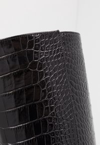 Sort ankelstøvle med en blank krokodillestruktur, der har en struktureret form og et elegant design. Ingen synlige beslag eller accenter.