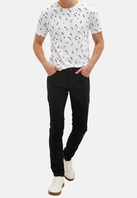 Bílé tričko s černým trojúhelníkovým vzorem, v kombinaci s černými džíny a bílými teniskami. Moderní střih, krátké rukávy, ležérní design.