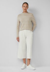 Beige gestreepte trui met een ronde hals, gecombineerd met witte cropped broek met wijde pijpen. Model draagt witte sneakers. Eenvoudig, strak ontwerp.