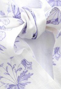 Hvidt stof med lyse lilla blomsterdesigns, snoet ind i en sløjfe. Texturen fremstår blød med detaljeret udformning af blomsterne.