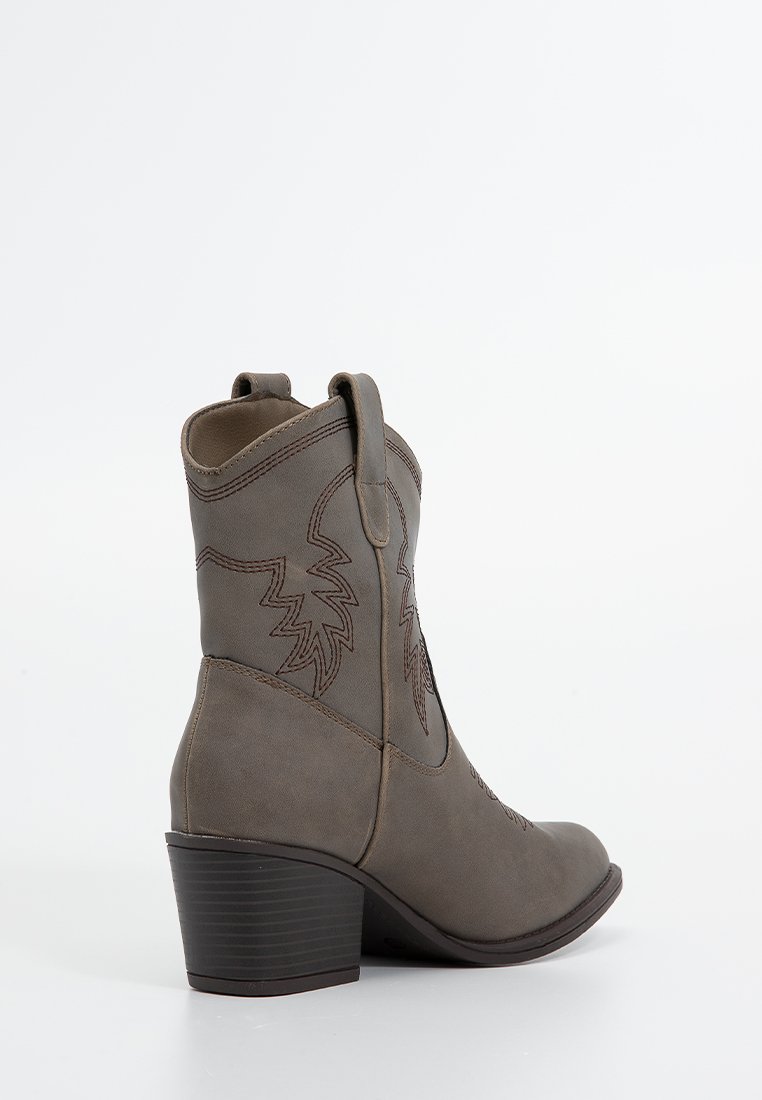 Bota de vaquero de cuero marrón con punta afilada, patrón de hojas bordado, lengüetas para tirar y tacón apilado. Textura suave y diseño estructurado.