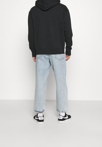 Sudadera con capucha negra, jeans de pierna ancha en azul claro y zapatillas negras con acentos blancos. Diseño simple con corte relajado y mangas con puños.