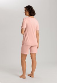 Ljust rosa pyjamas med kortärmad topp och shorts, båda med vågig kant. Mjukt tyg med avspänt snitt och enkel design.
