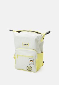 En ljusgrå och gul ryggsäck har en top drawstring-stängning och en framficka med dragkedja, märkt med ordet "HUNTER."