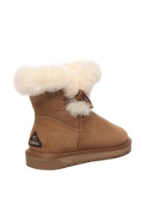 Brown suede ankle boot with cream fur trim, featuring a button closure and a rubber sole. Logo patch on the back. Rounded toe design.