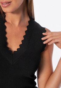 Top nero a coste con scollatura a V ondulata e bordi delle spalle, con texture liscia e design aderente.