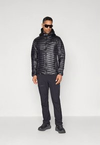 Svart isolert dunjakke med hette, glidelås foran og horisontal quilting, kombinert med svarte bukser og sportssko.