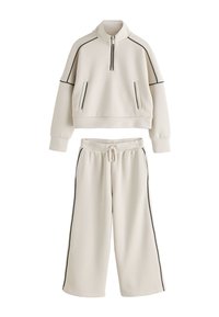 Cream-colored athletic set comprising a cropped pullover with half-zip and black piping, paired with wide-leg sweatpants with drawstring.