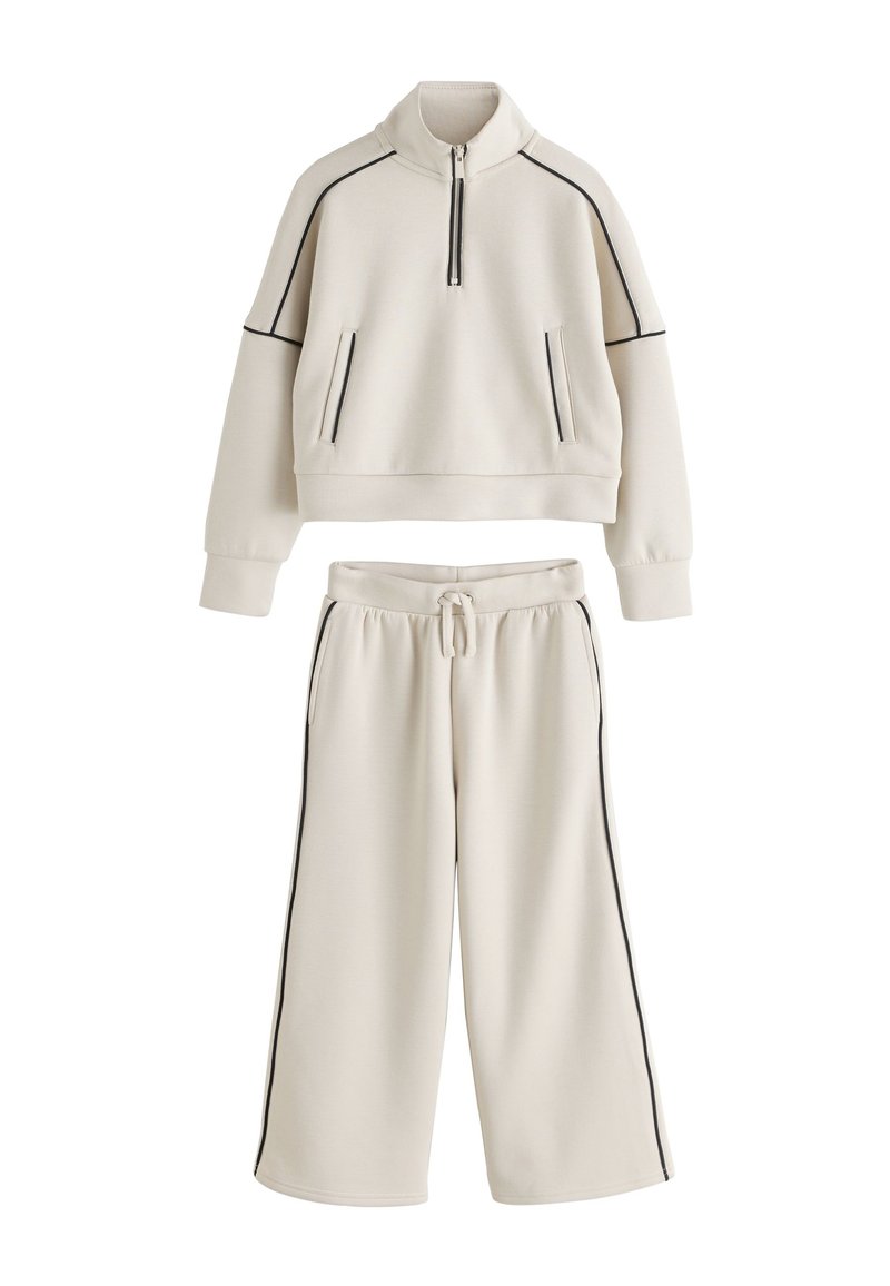 Cream-colored athletic set comprising a cropped pullover with half-zip and black piping, paired with wide-leg sweatpants with drawstring.
