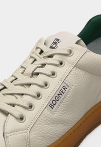 Baskets en cuir blanc texturé avec lacets beige, doublure intérieure verte, semelle marron, et un logo argenté en forme de "B" au-dessus de l'étiquette "BOGNER" sur le côté.