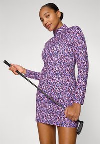 Abito aderente a maniche lunghe di colore viola con stampa leopardata multicolore. Realizzato in tessuto elasticizzato, abbinato a un golf club in mano.