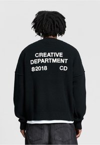 Black knitted sweater featuring oversized fit, ribbed texture, and bold white text “CREATIVE DEPARTMENT 2018 CD” on the back.